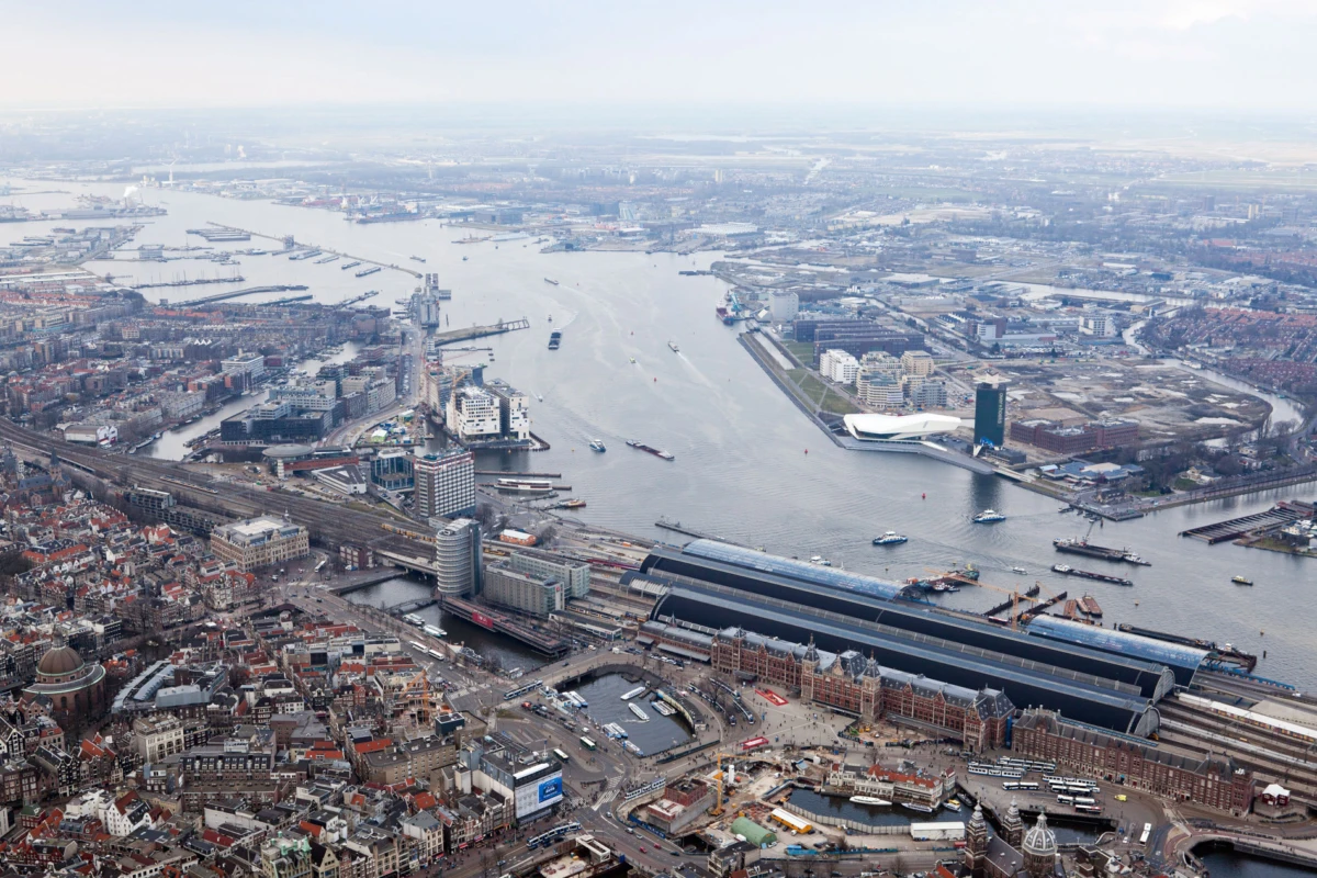 Aerial view of Rotterdam port and cityscape with ships, warehouses, and railway station.