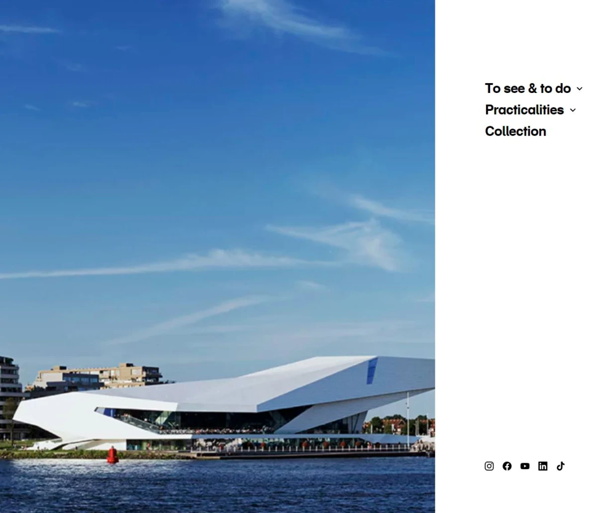 White angular contemporary building by a waterfront promenade under a clear blue sky.