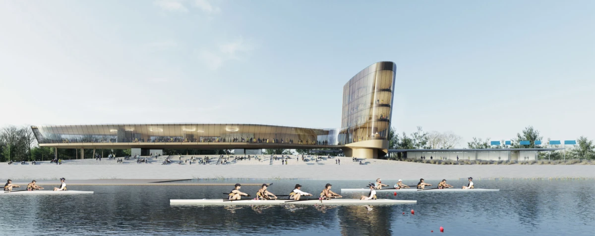 Rowers in racing shells glide on a calm river beside a modern glass building with a curved tower.