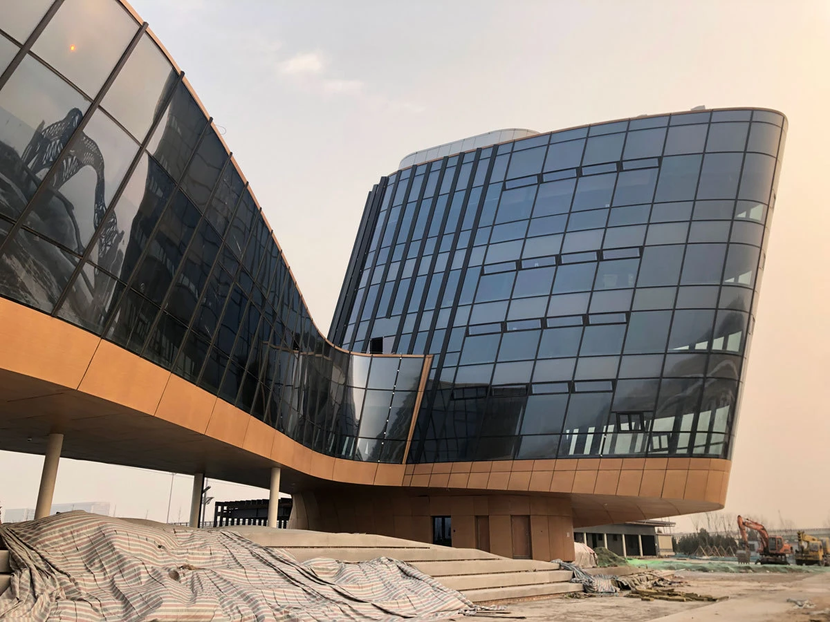 Modern curved glass office building under construction; tarps on the foreground and construction equipment in the background.
