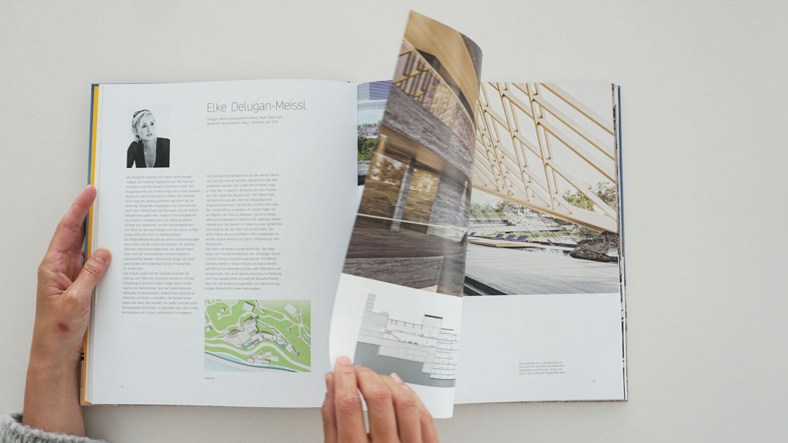 Hands turn a large open design magazine on a white surface, exposing architectural photos and article text.