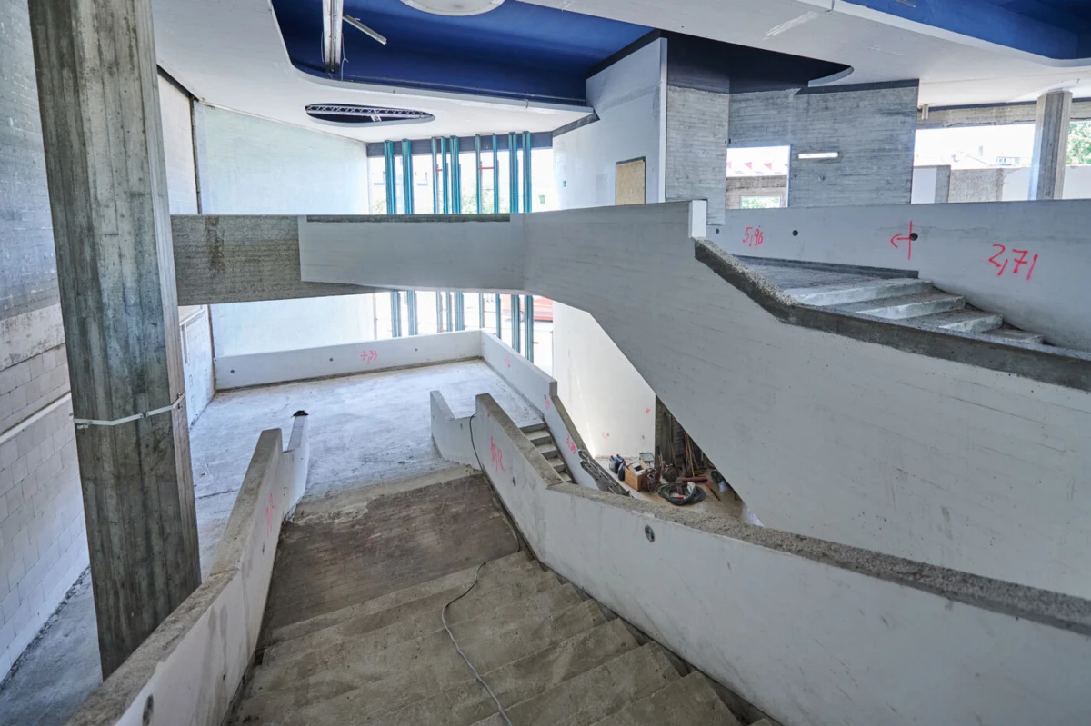 Interior of an unfinished building featuring a concrete staircase with multiple levels, exposed column, and scattered construction debris.