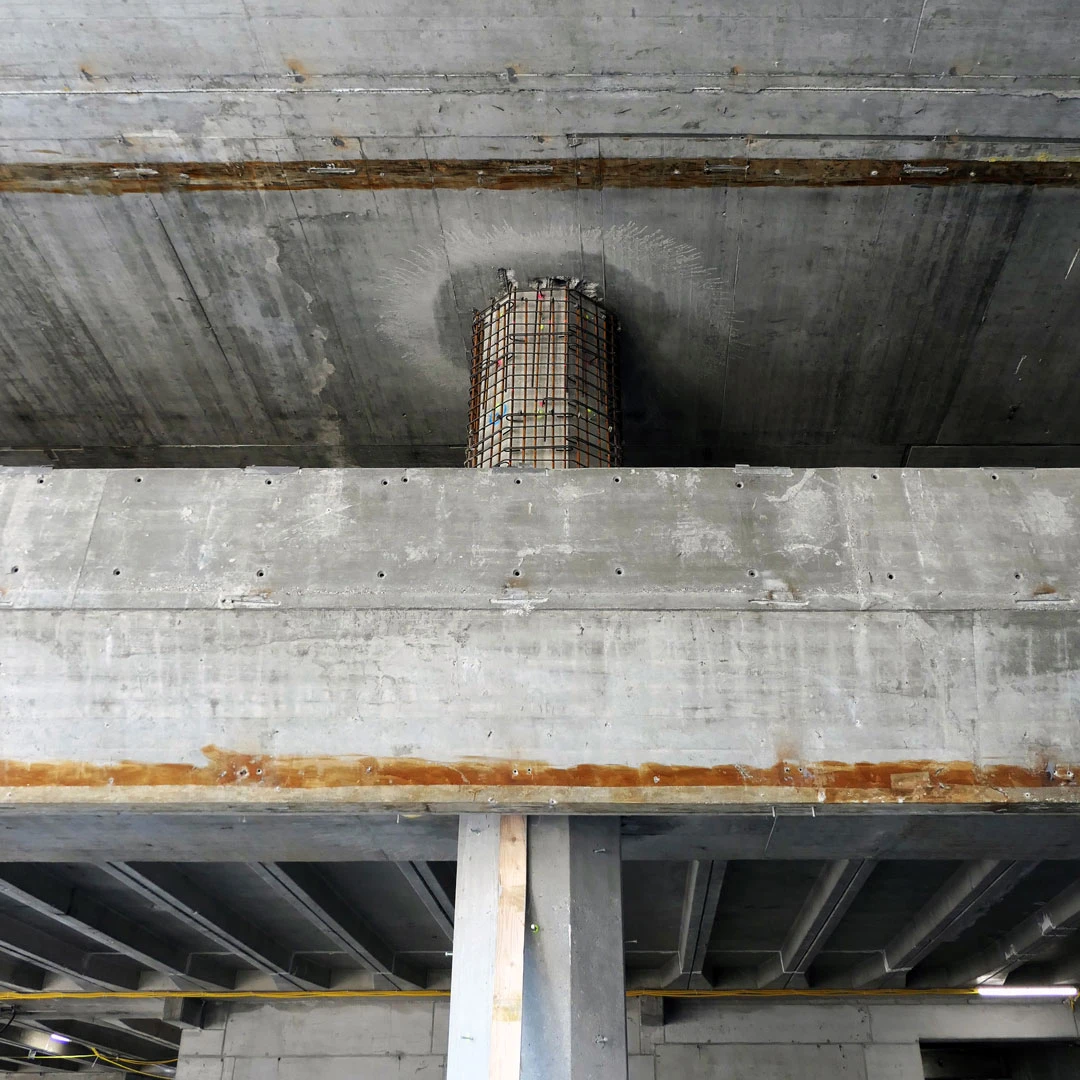 Rusty steel rebar cage protrudes from a circular concrete shaft in an industrial construction site.