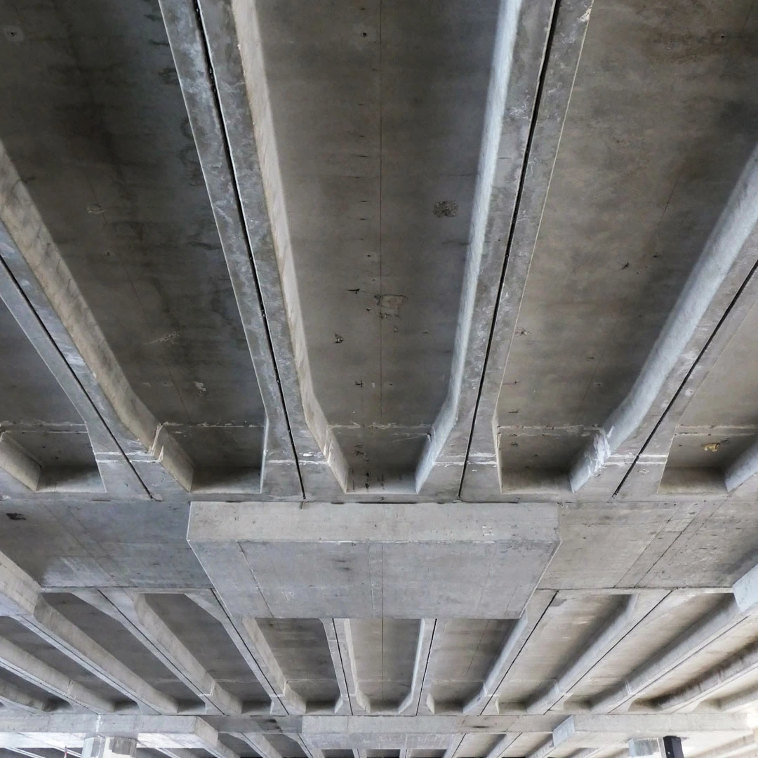 Underside of a concrete overpass showing parallel support beams and cross girders, viewed from below.