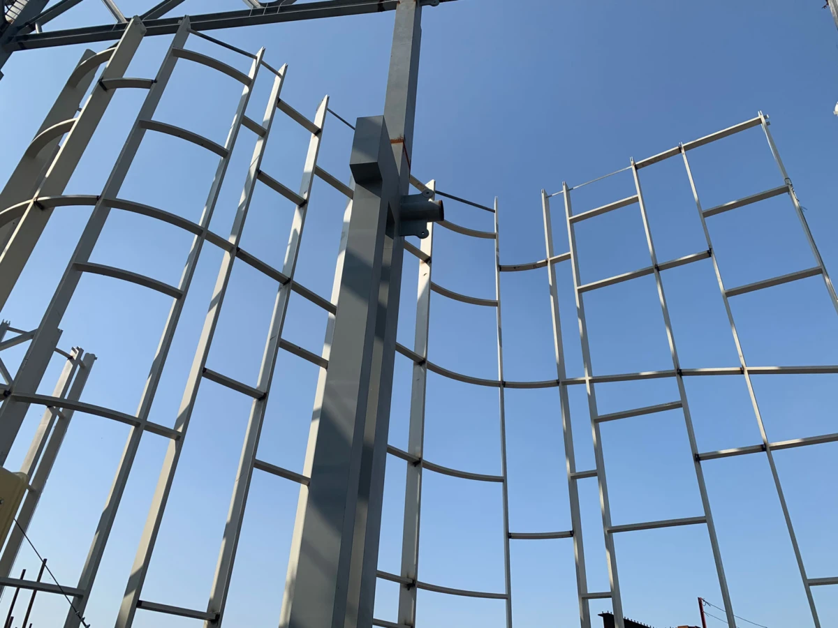 Industrial steel framework with curved rails forming a wave-like sculpture, outdoors against a clear blue sky.