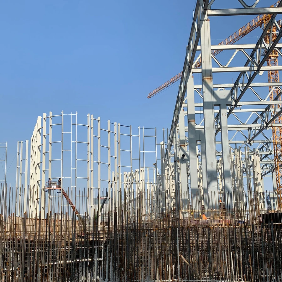 Construction site with a steel framework being erected; workers on a suspended platform among vertical columns under a blue sky