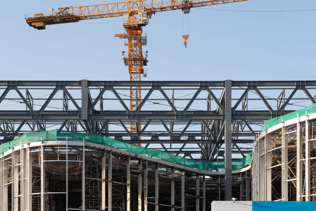 Orange tower crane over a steel lattice framework under construction; curved sections with green safety netting.