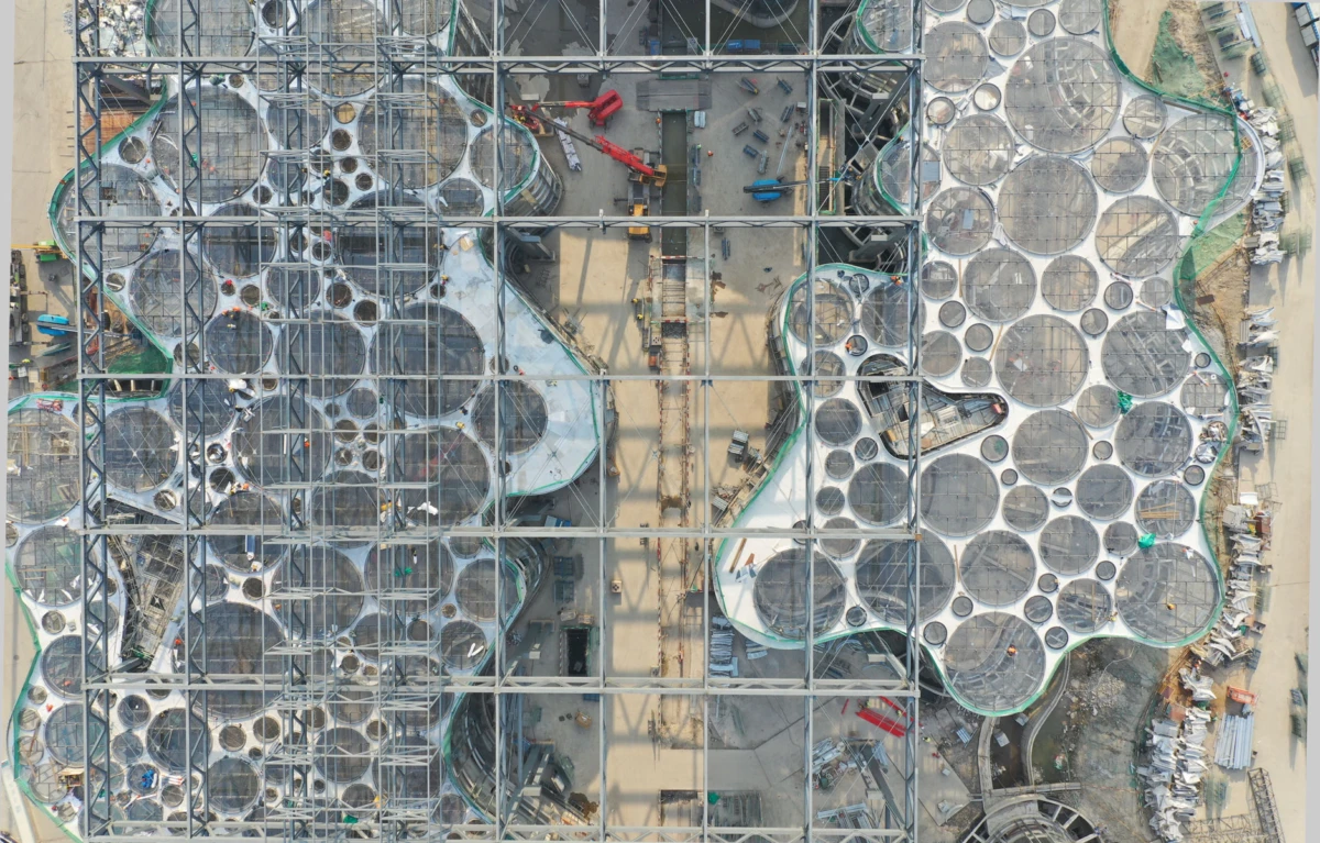 Aerial view of a construction site with a steel frame and numerous circular concrete formwork panels across the roof.