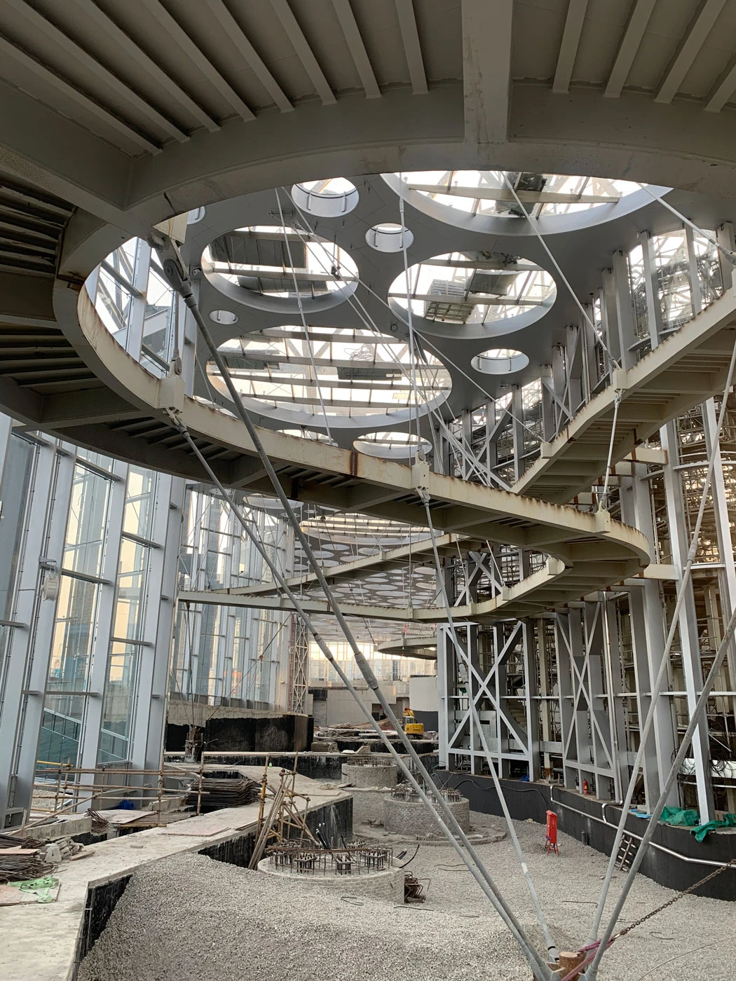Spiraling steel staircase with circular landings inside a glass-walled construction site with scaffolding.