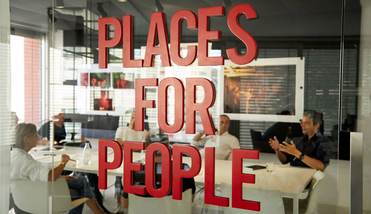 Glass-walled conference room with people around a table in discussion; red PLACES FOR PEOPLE sign on the glass