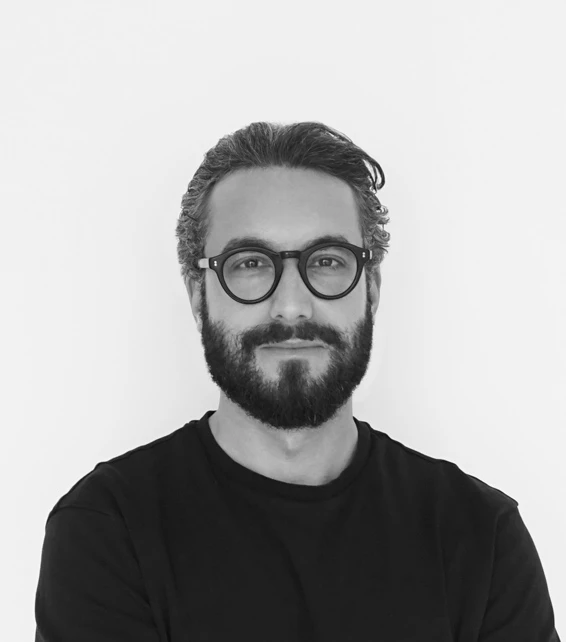 Bearded man with round glasses facing the camera against a plain white background.