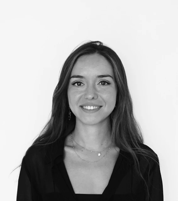 Smiling young woman with long hair wearing a black blouse, facing the camera against a plain white background.