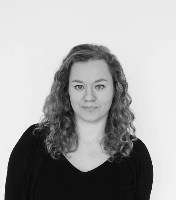 Portrait of a person with curly shoulder-length hair, looking at the camera, wearing a black top against a plain light background.