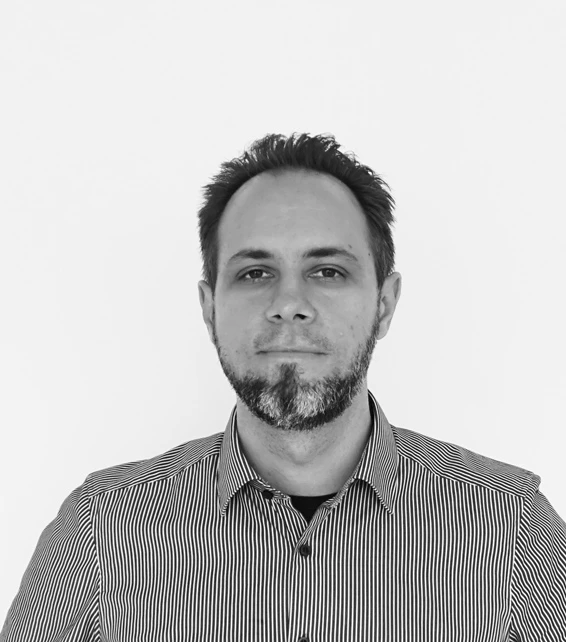 Black-and-white portrait of an adult with short dark hair and trimmed beard, wearing a striped shirt, facing the camera against a plain background.