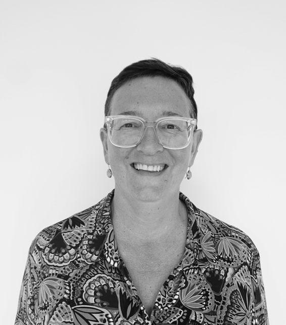 Smiling person wearing clear-framed glasses and a patterned shirt, against a plain white background.