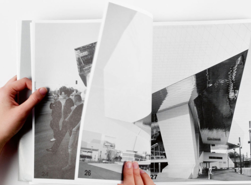 Hands turn pages of a black-and-white photo album on a white surface, showing a modern architectural building.