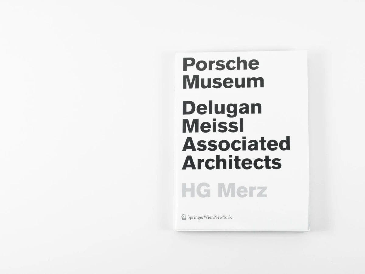 White book cover with bold black text reading Porsche Museum Delugan Meissl Associated Architects HG Merz on a white surface.