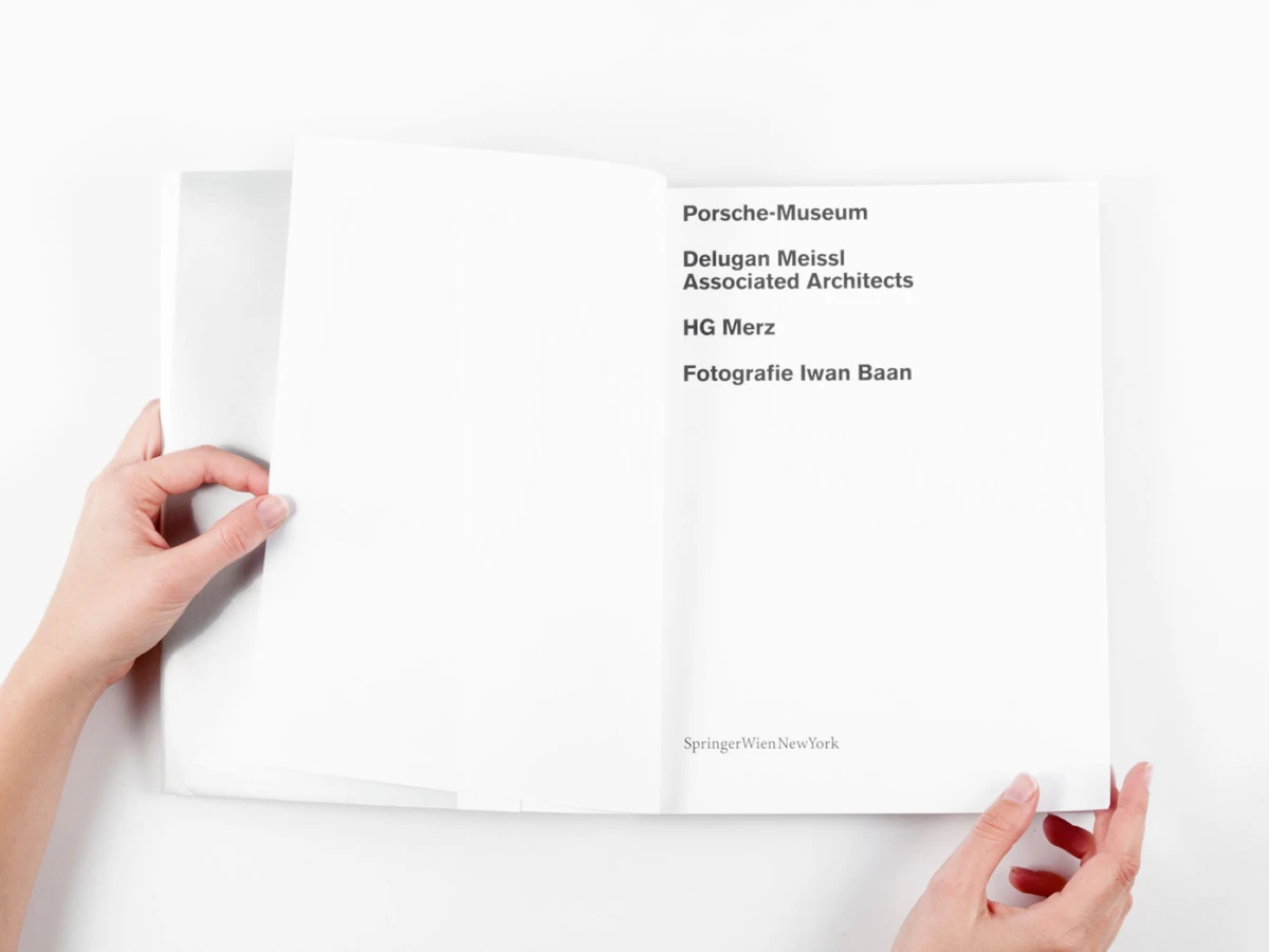 Open white book held by hands; right page lists credits: Porsche-Museum, Delugan Meissl Associated Architects, HG Merz, Fotografie Iwan Baan.