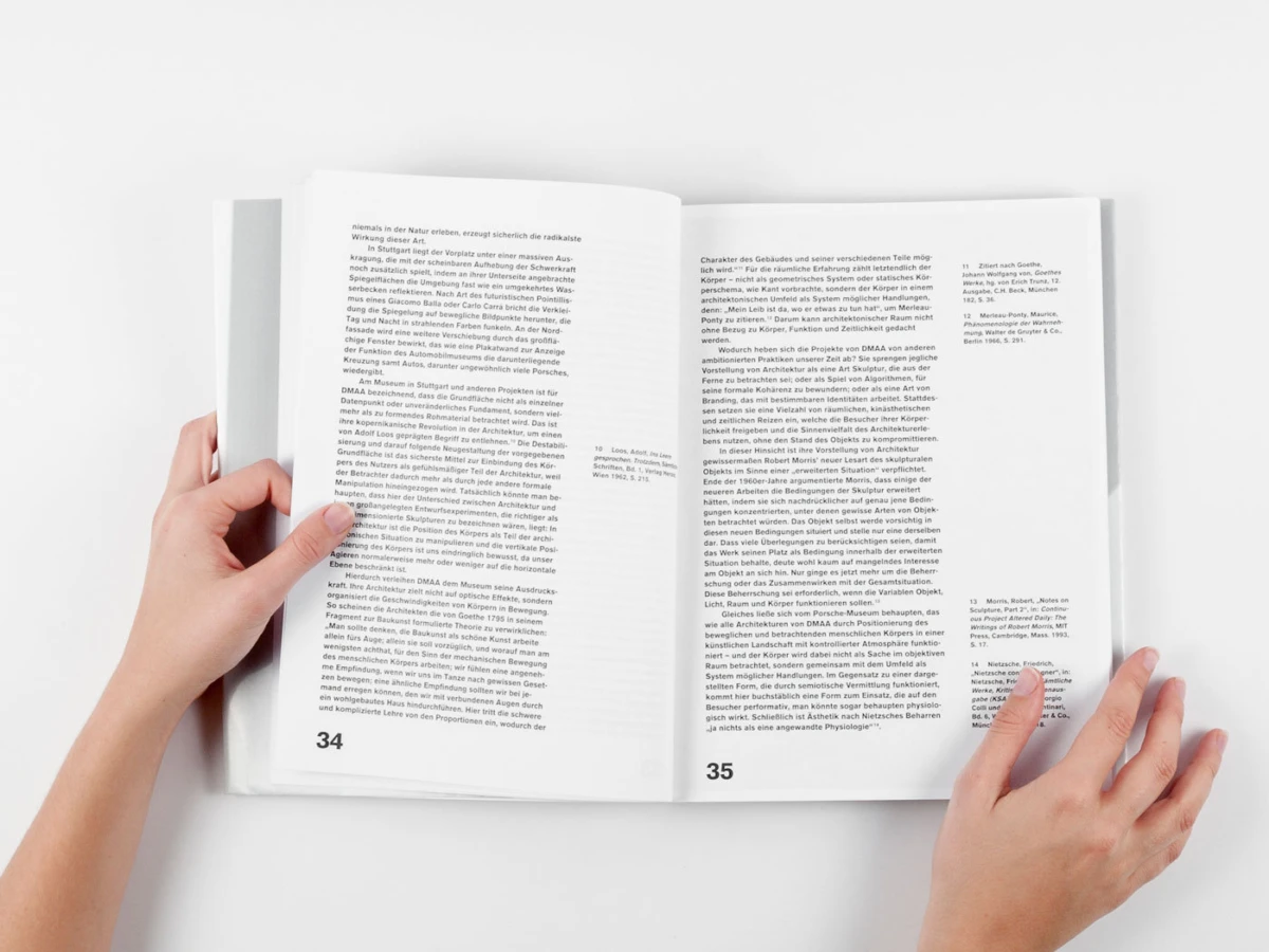 Two hands turn the pages of an open magazine spread on a white surface.