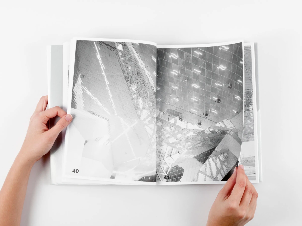 Two hands hold open photo book showing a black-and-white architectural interior spread; pages 40–41 visible.