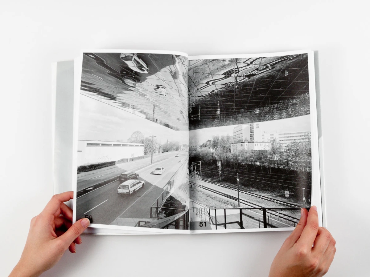 Hands hold open photo book showing a black-and-white urban scene with cars on a street beneath an elevated railway.