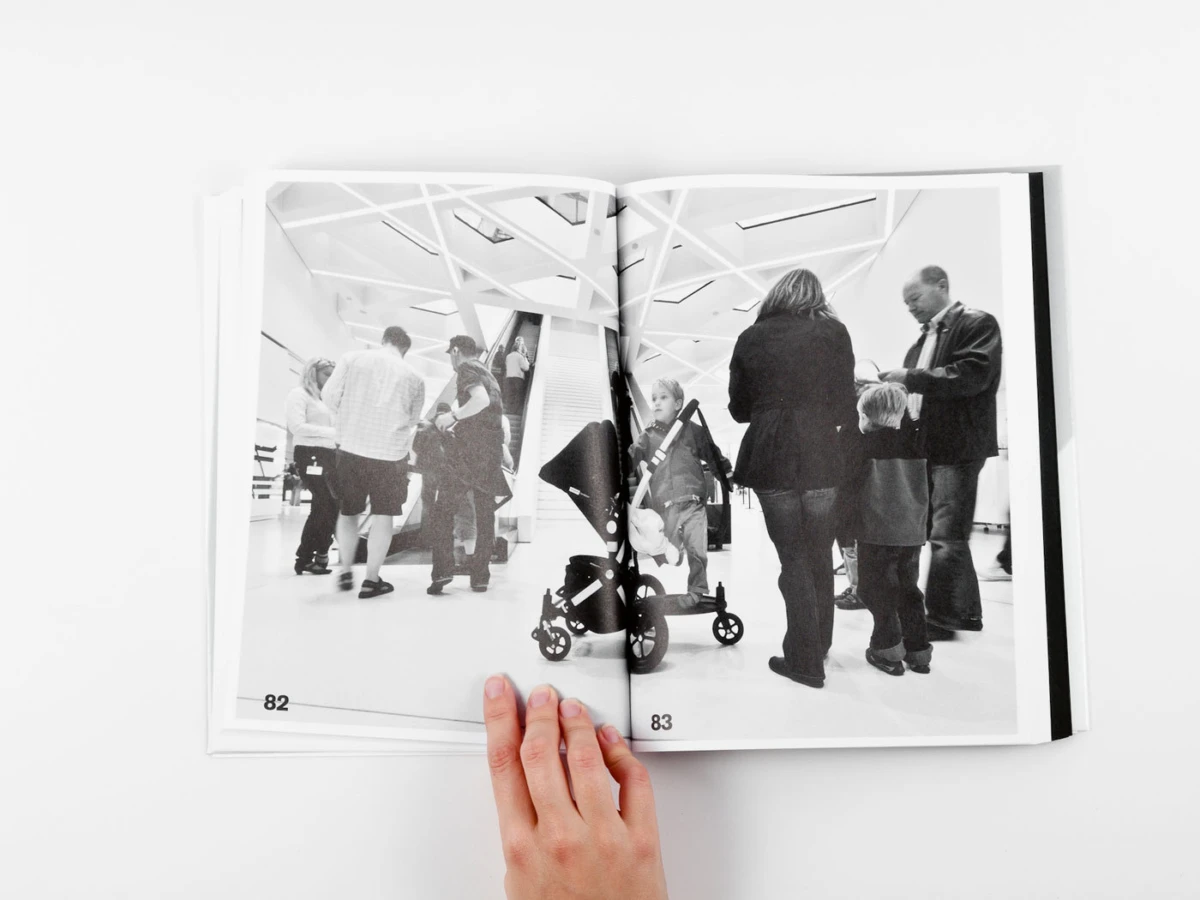 Open book showing a black-and-white photo of a crowd in a bright, geometric interior; a person pushes a stroller at the center.