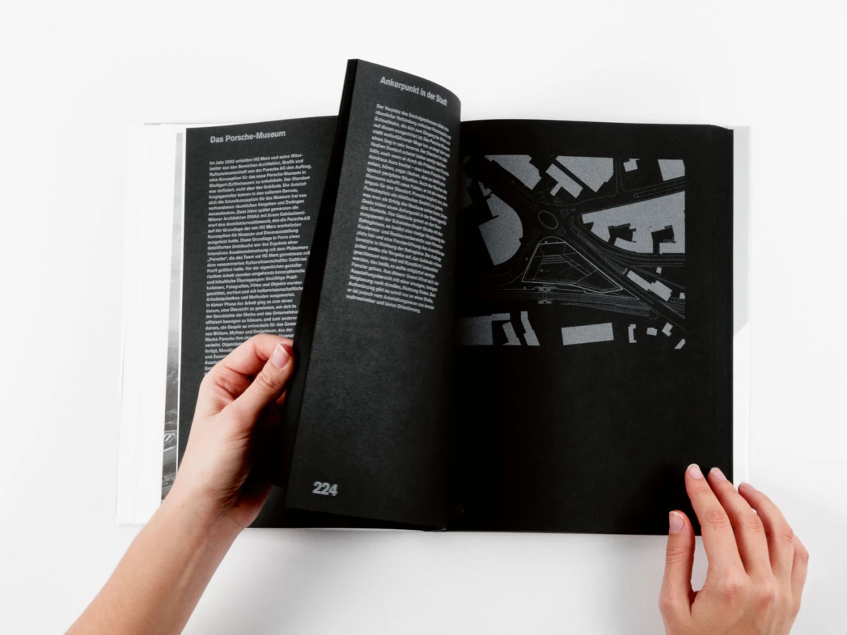 Pair of hands flipping through a black art book with white text and a monochrome diagram on a white surface.