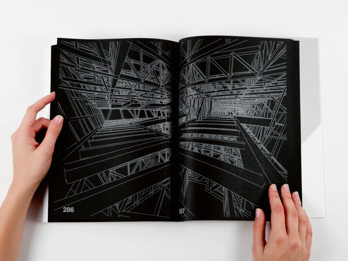 Open book with black pages, intricate white line drawing of intersecting structural beams; two hands hold the pages.