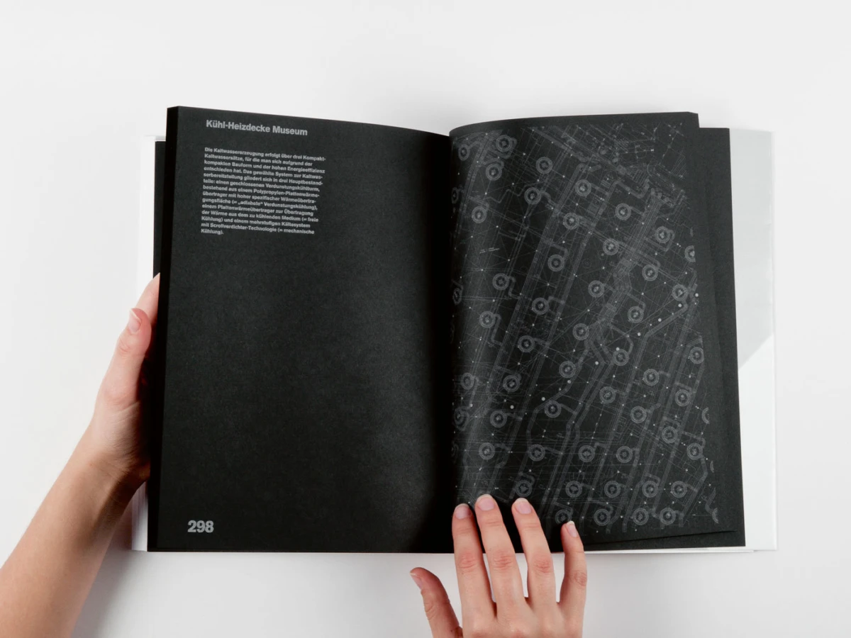 Hands holding open book with black pages on a white surface; left page contains small text, right page shows a gray circuitry pattern.