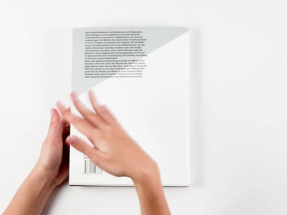 Two hands slide across a plain white hardcover book on a white background.