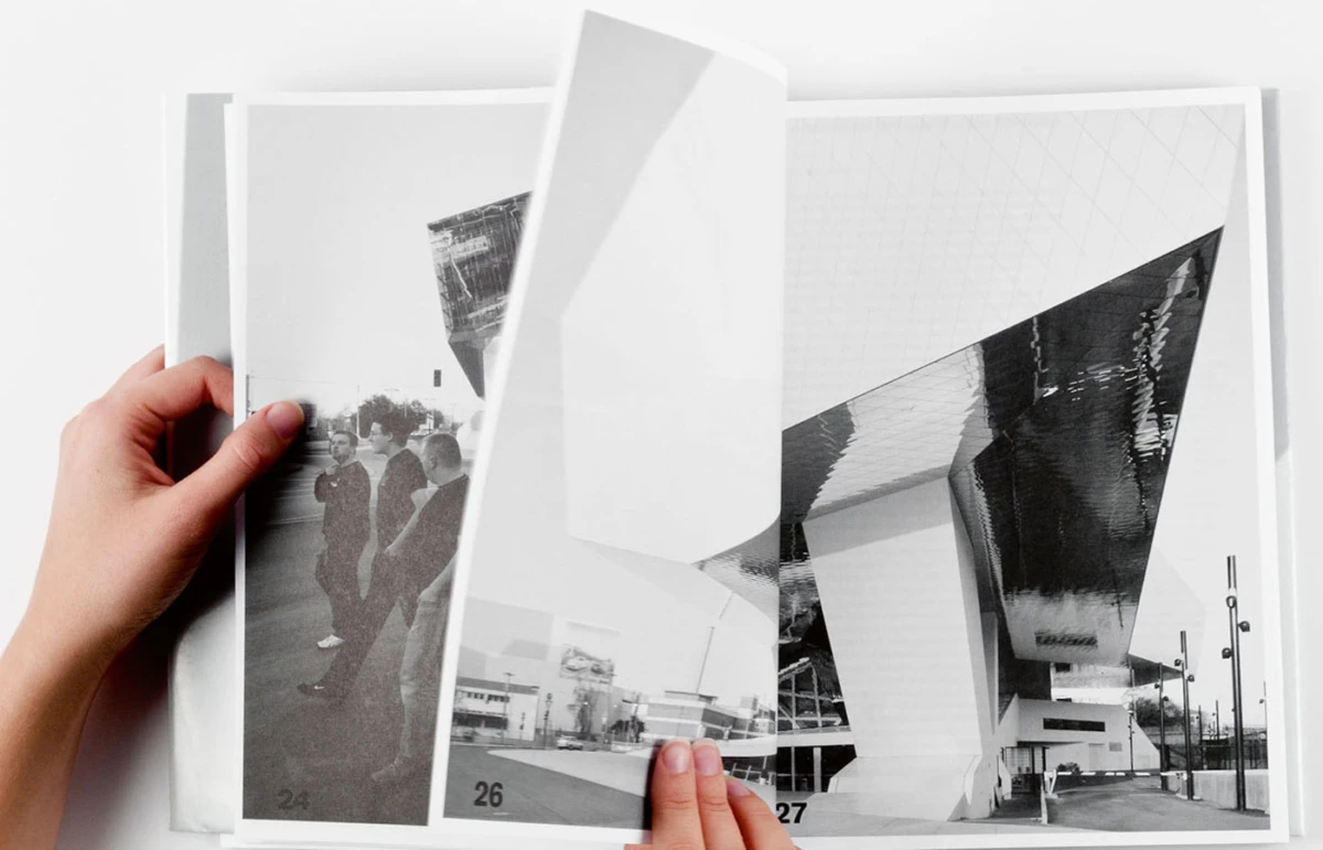 Hands turn pages of a black-and-white photo album on a white surface, showing a modern architectural building.