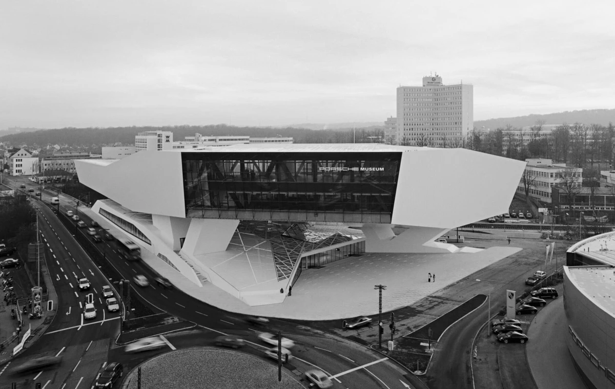 Porsche Museum exterior, a futuristic white angular building, at a busy urban intersection with cars.