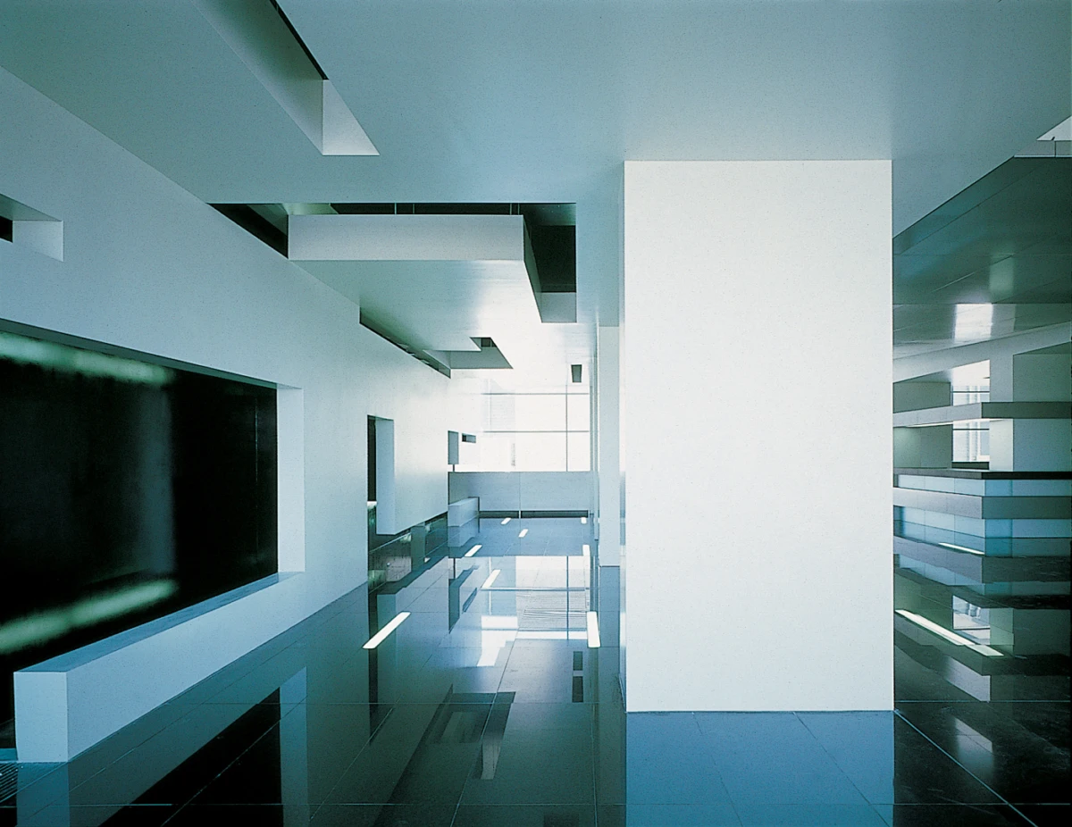 Empty modern interior atrium with a tall white rectangular pillar, glass railing, and a reflective glossy floor.