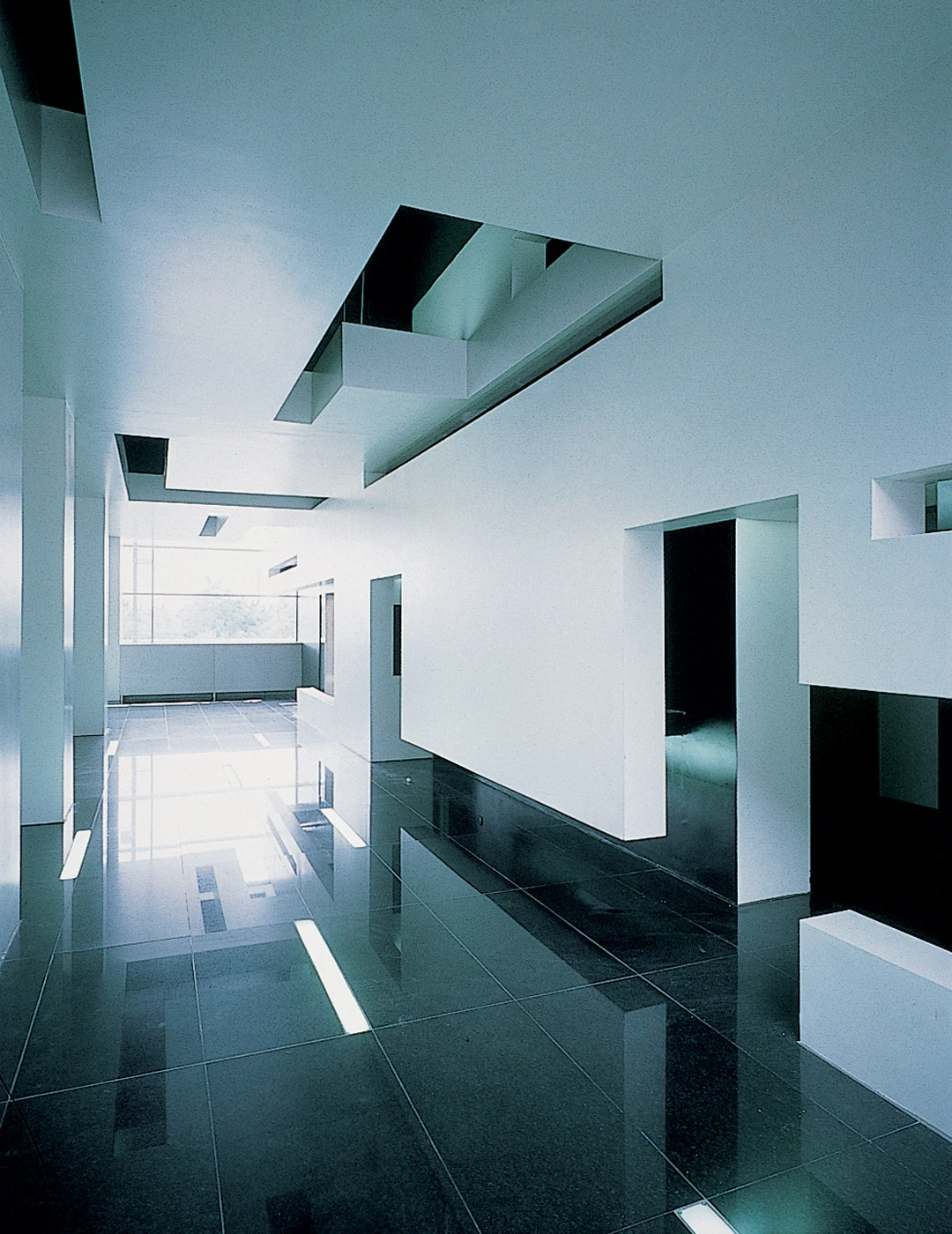 Empty minimalist modern interior hallway with white walls, black glossy floor, and geometric ceiling openings.
