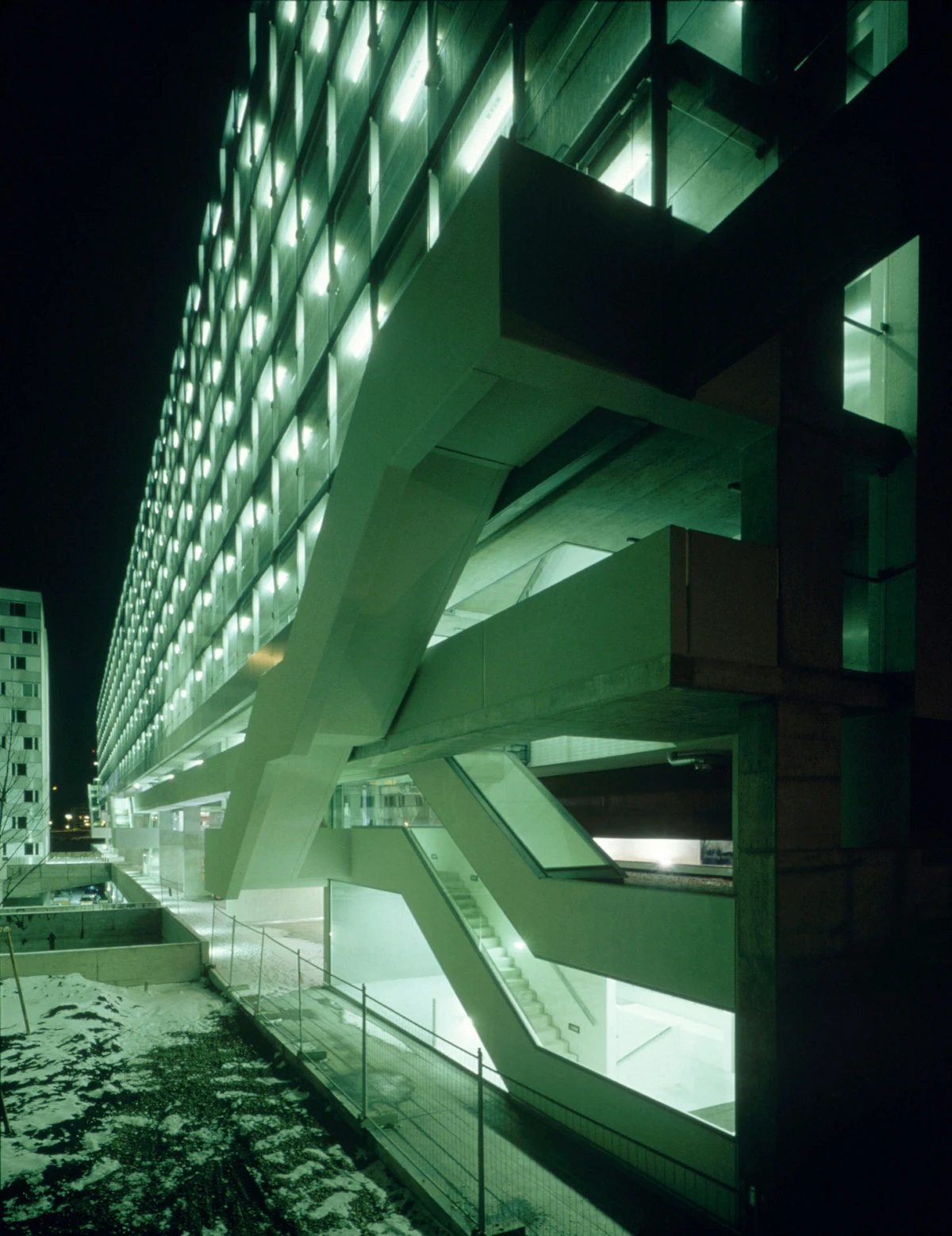 Nighttime view of a concrete parking garage with illuminated diagonal ramps and green lighting.