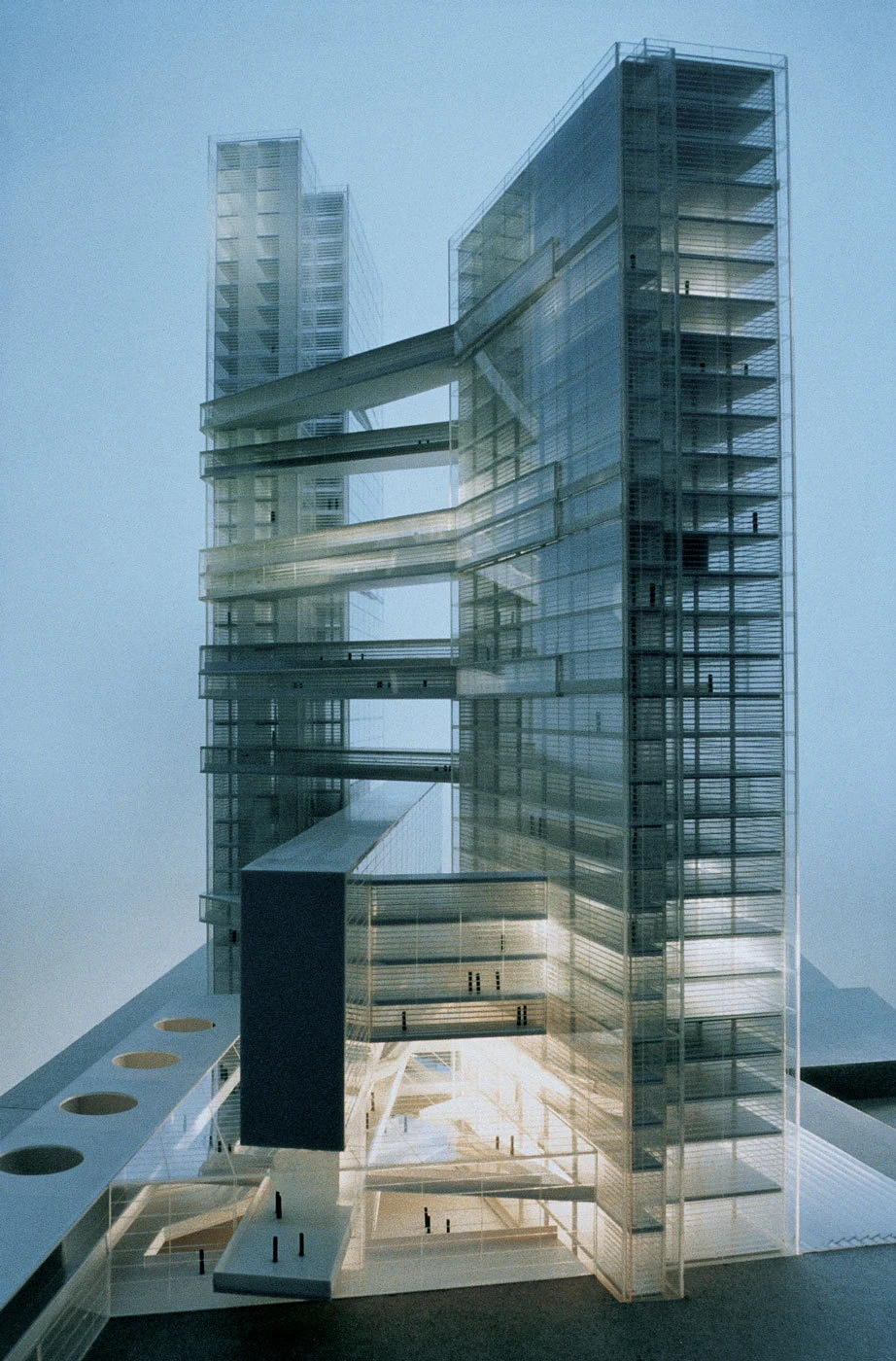 Scale architectural model of glass skyscraper connected by skybridges between towers, displayed on a white platform.