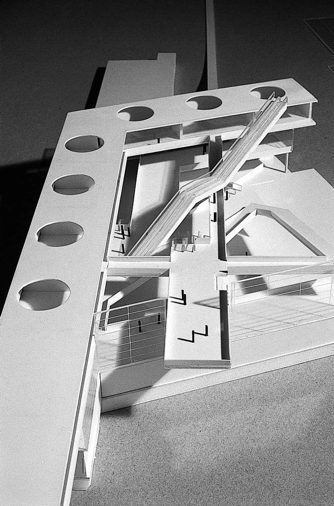 Scale architectural model of a multi-level structure featuring ramps, stairways, railings, and a diagonally placed beam with circular cutouts.