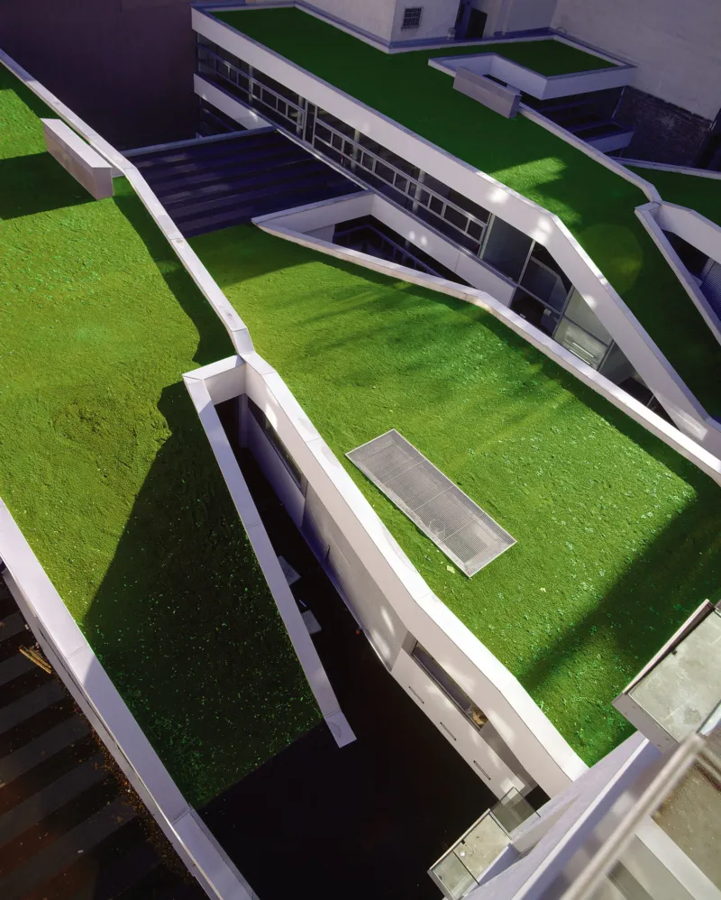 Aerial view of a modern building complex with green rooftops and white angular walkways.