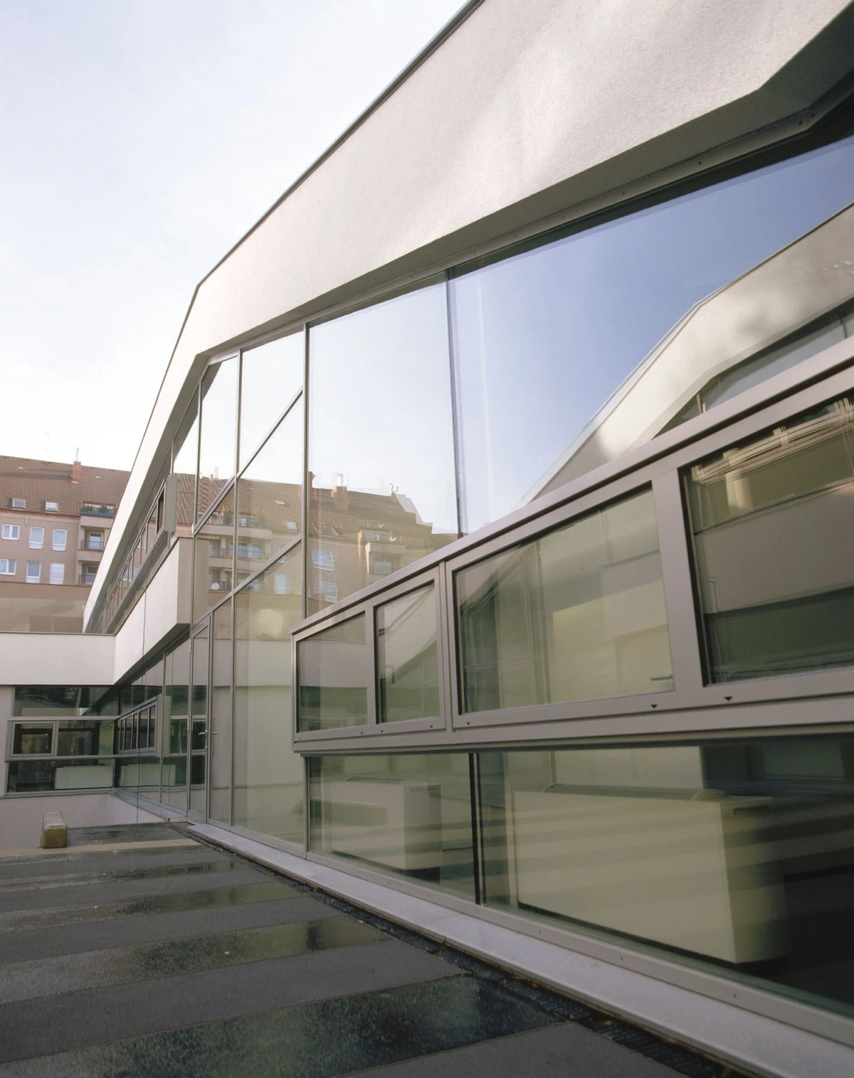 Contemporary office building exterior with large glass windows, reflecting surrounding cityscape; urban daytime setting.