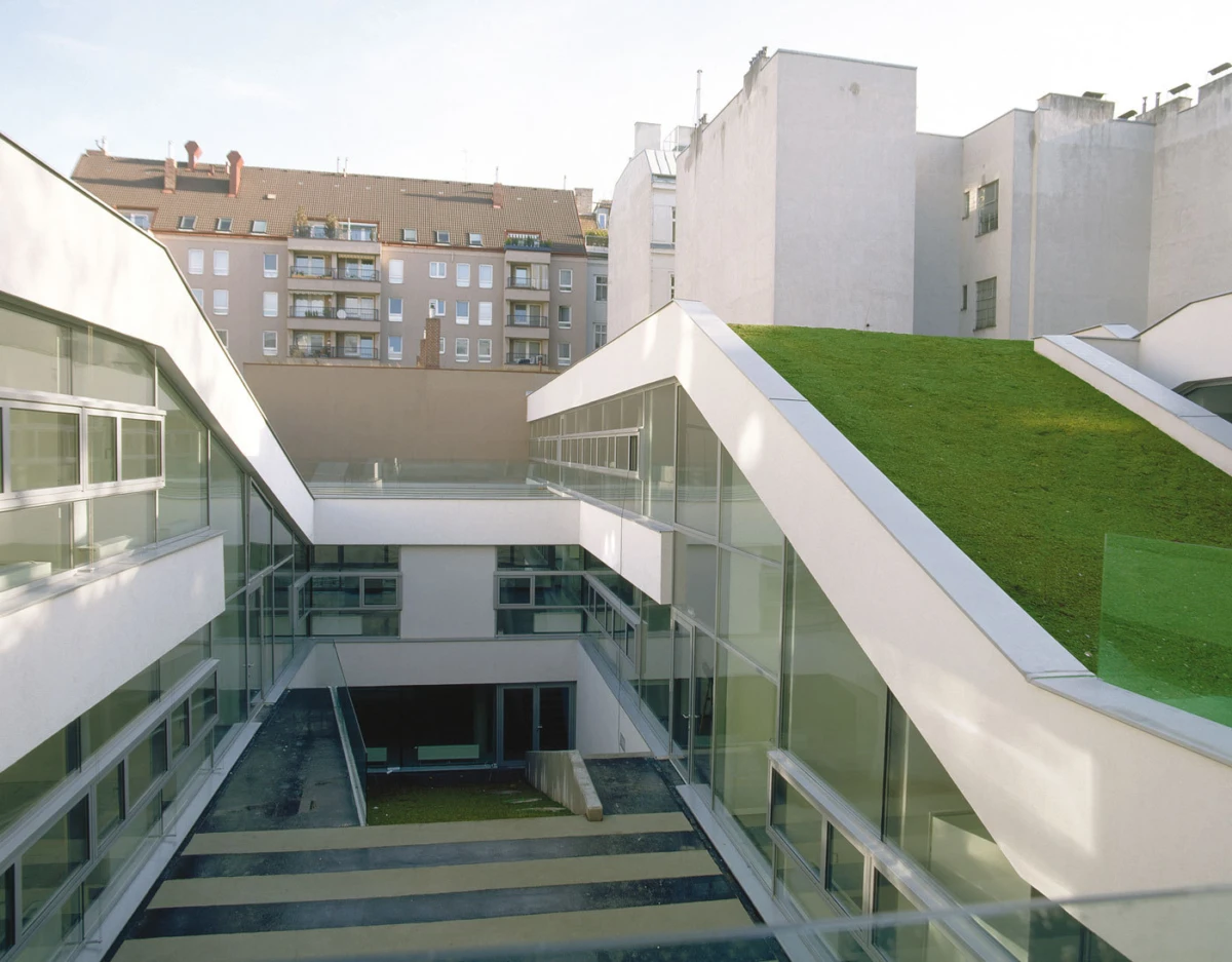 Modern glass-walled courtyard with elevated walkways and a green roof on the right.