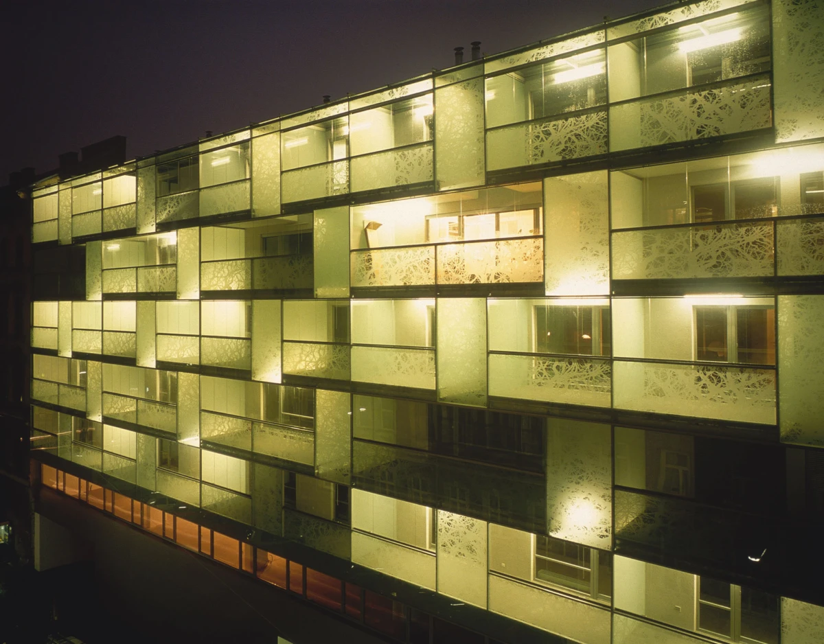 Nighttime view of a modern apartment building with illuminated glass balconies and frosted decorative panels.