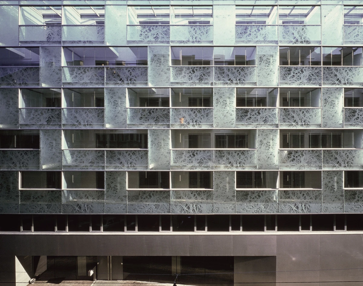 Modern multistory office building façade featuring repeating rectangular bays with ornate perforated metal screens.