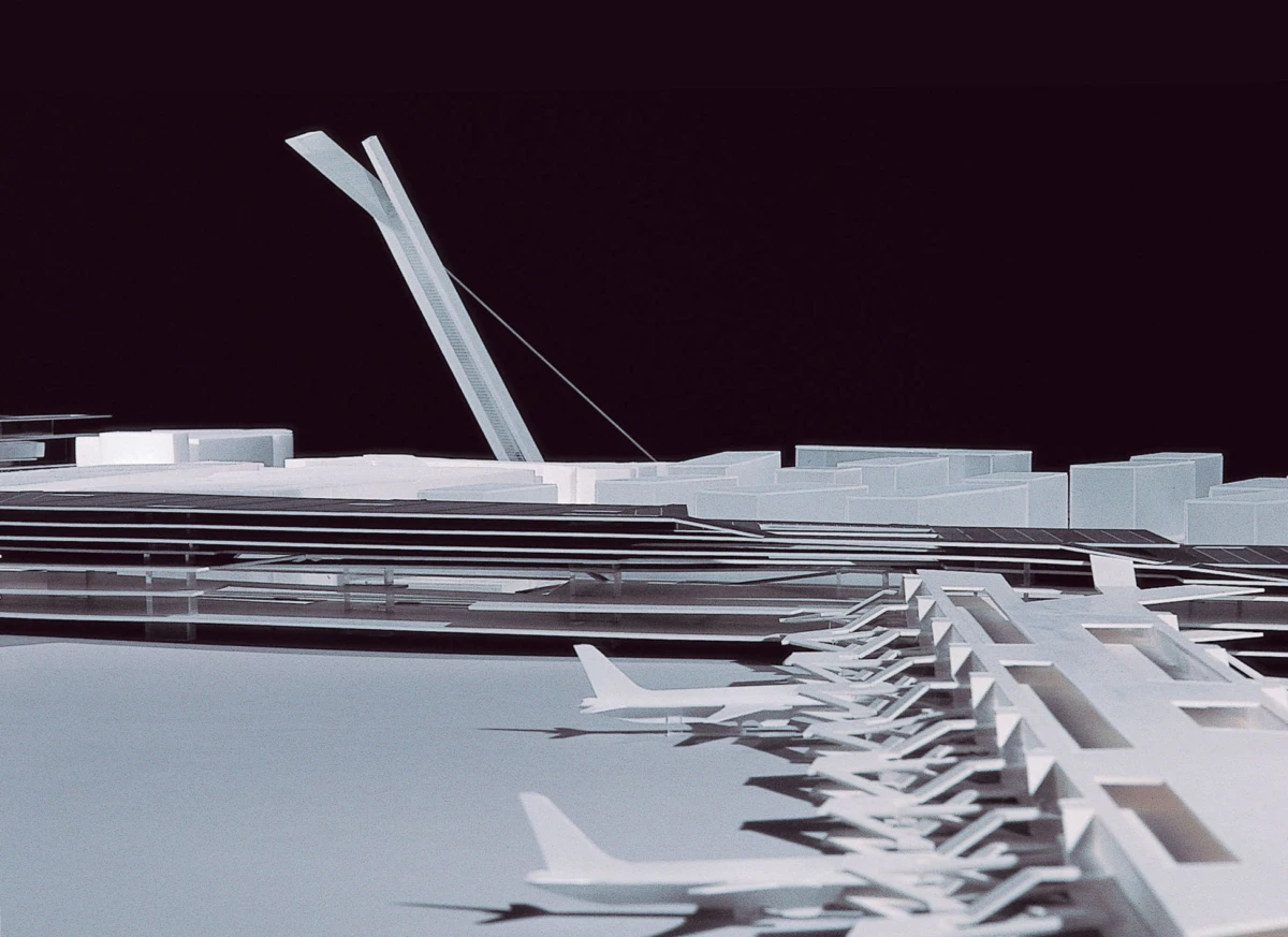Static white architectural model of an airport terminal with jet bridges and airplanes at gates, nighttime.