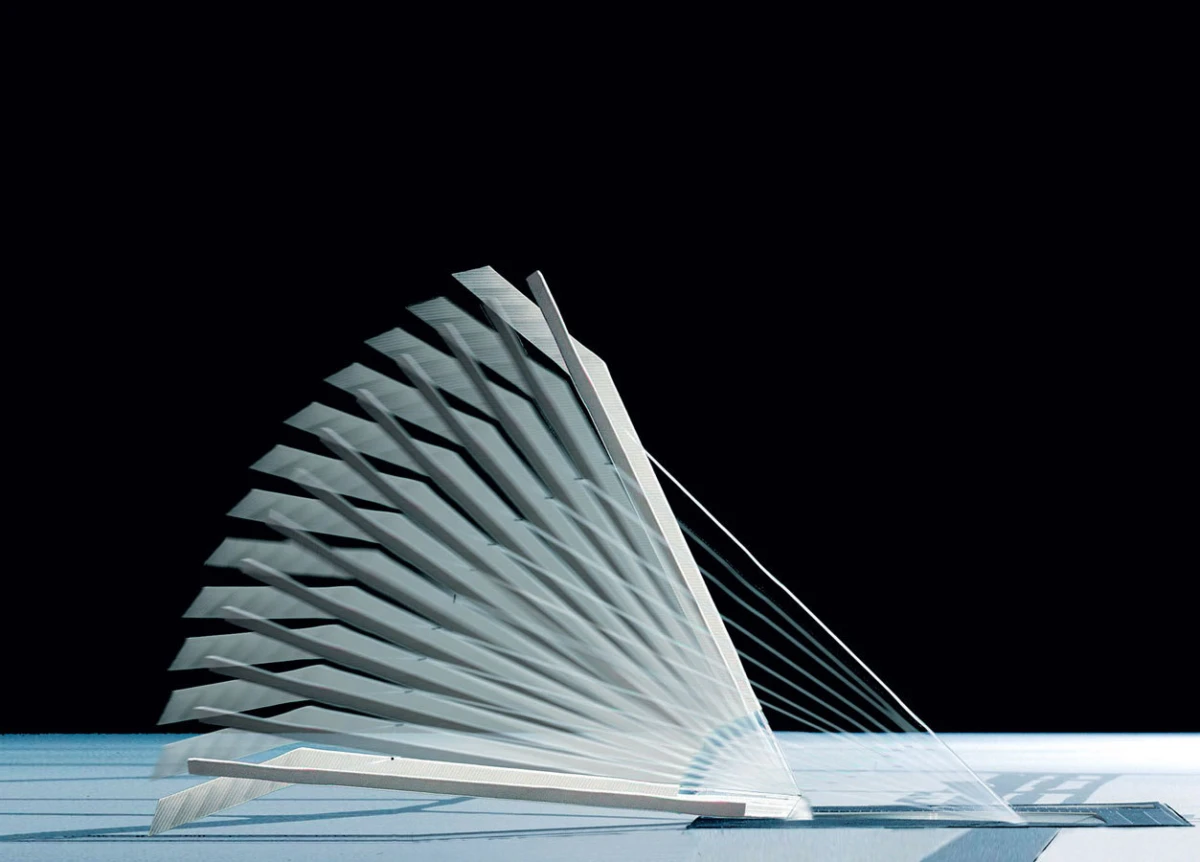 White sail-shaped tensile structure with curved blades and cables, set on a flat surface against a dark sky.