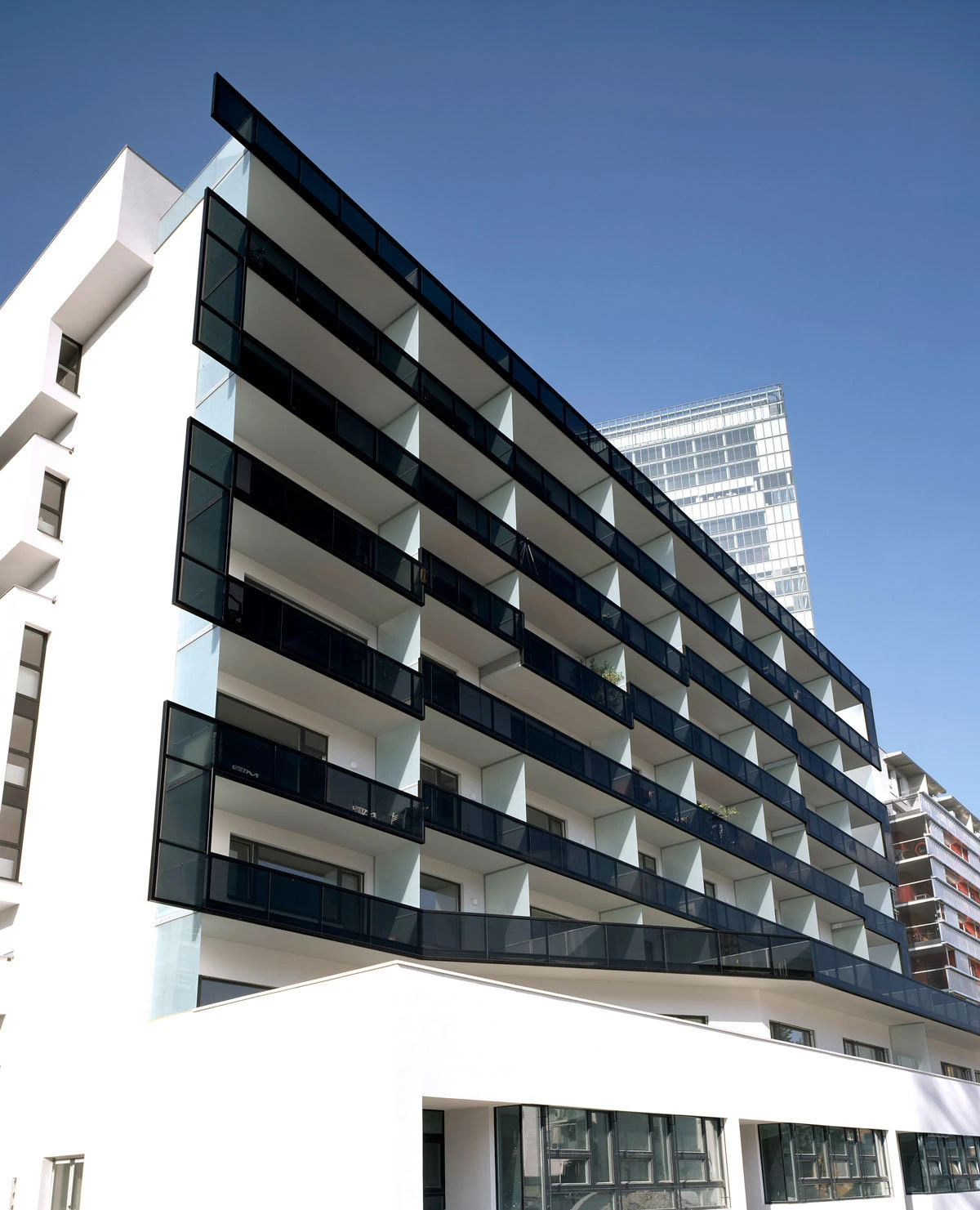 Front view of a multi-story white apartment building with glass balcony railings in an urban skyline.