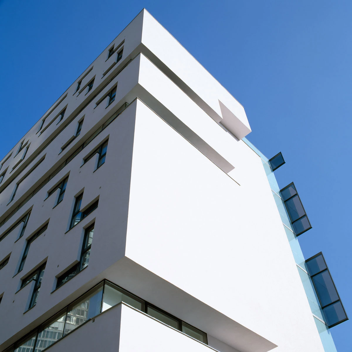 White modern apartment building with cantilevered balconies against blue sky.
