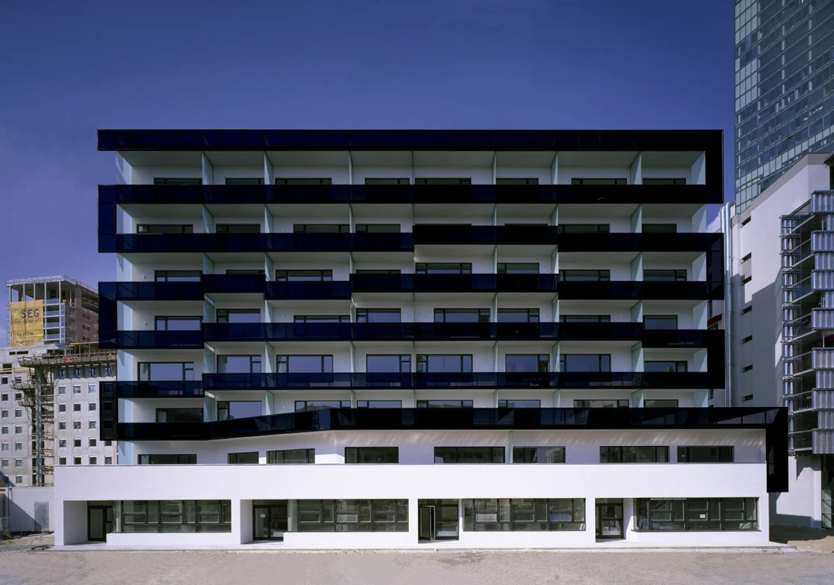 Modern white and black apartment building with stacked balconies in an urban setting.