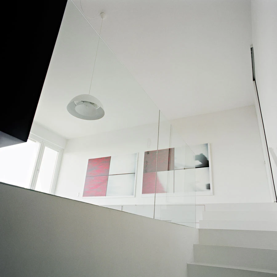 White modern interior with glass-railed staircase, circular pendant light, and four-panel abstract artwork.