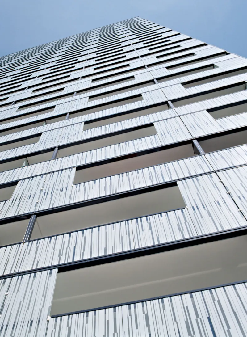 Viewed from street level, a tall modern high-rise with a striped facade and rectangular windows against a blue sky.