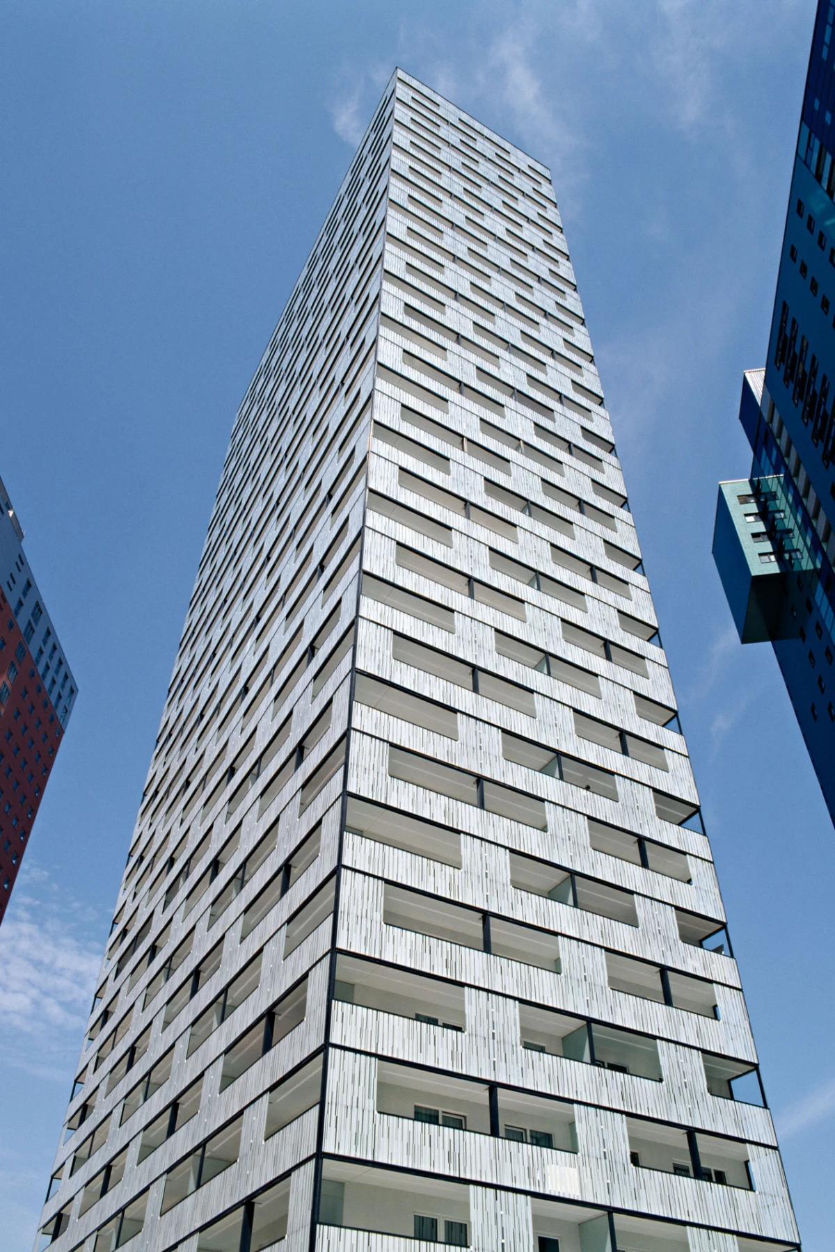 Tall white residential high-rise with a grid of rectangular windows, seen from street level against a blue sky